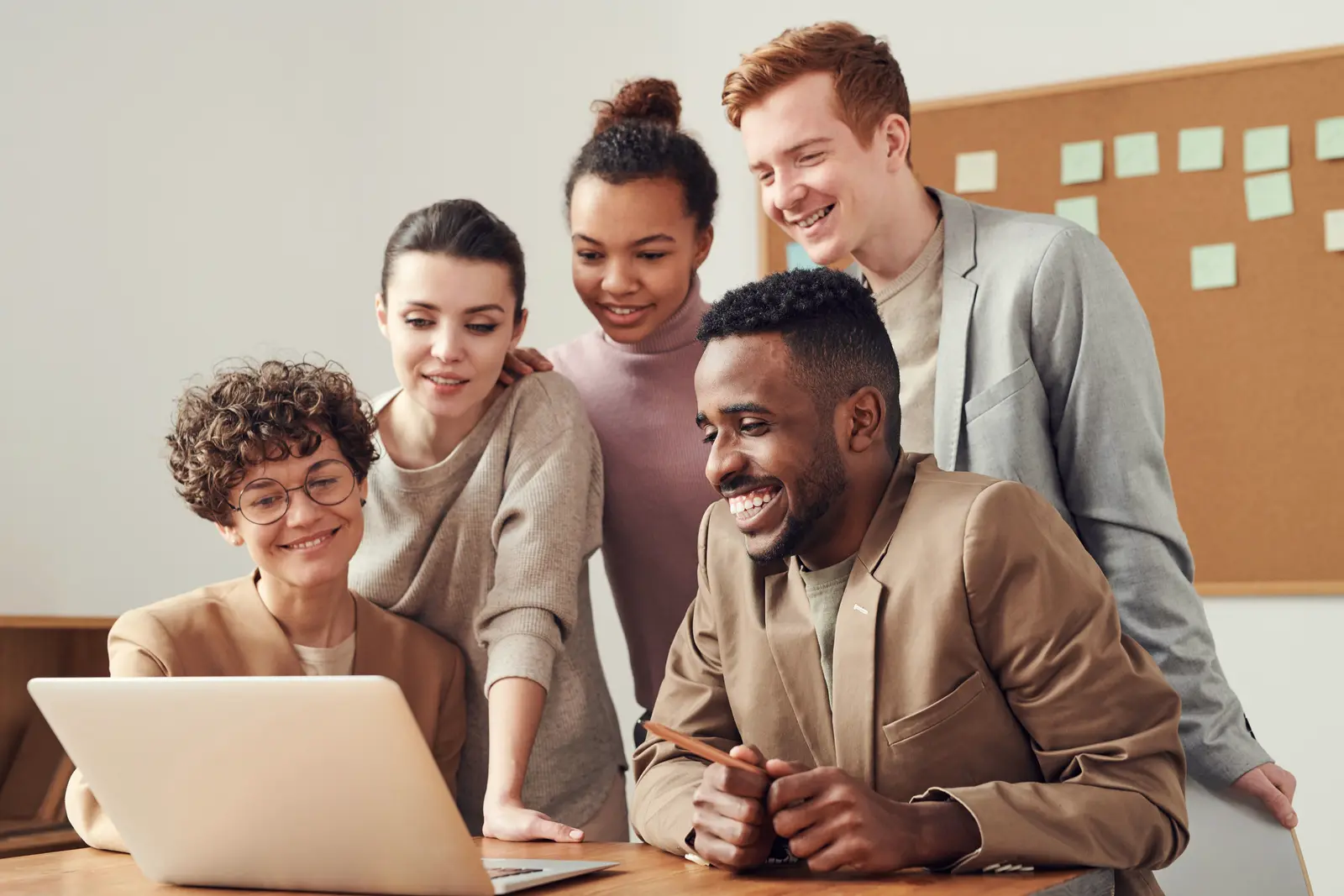 A mixed team standing around a laptop, looking at a screen the camera cannot read.