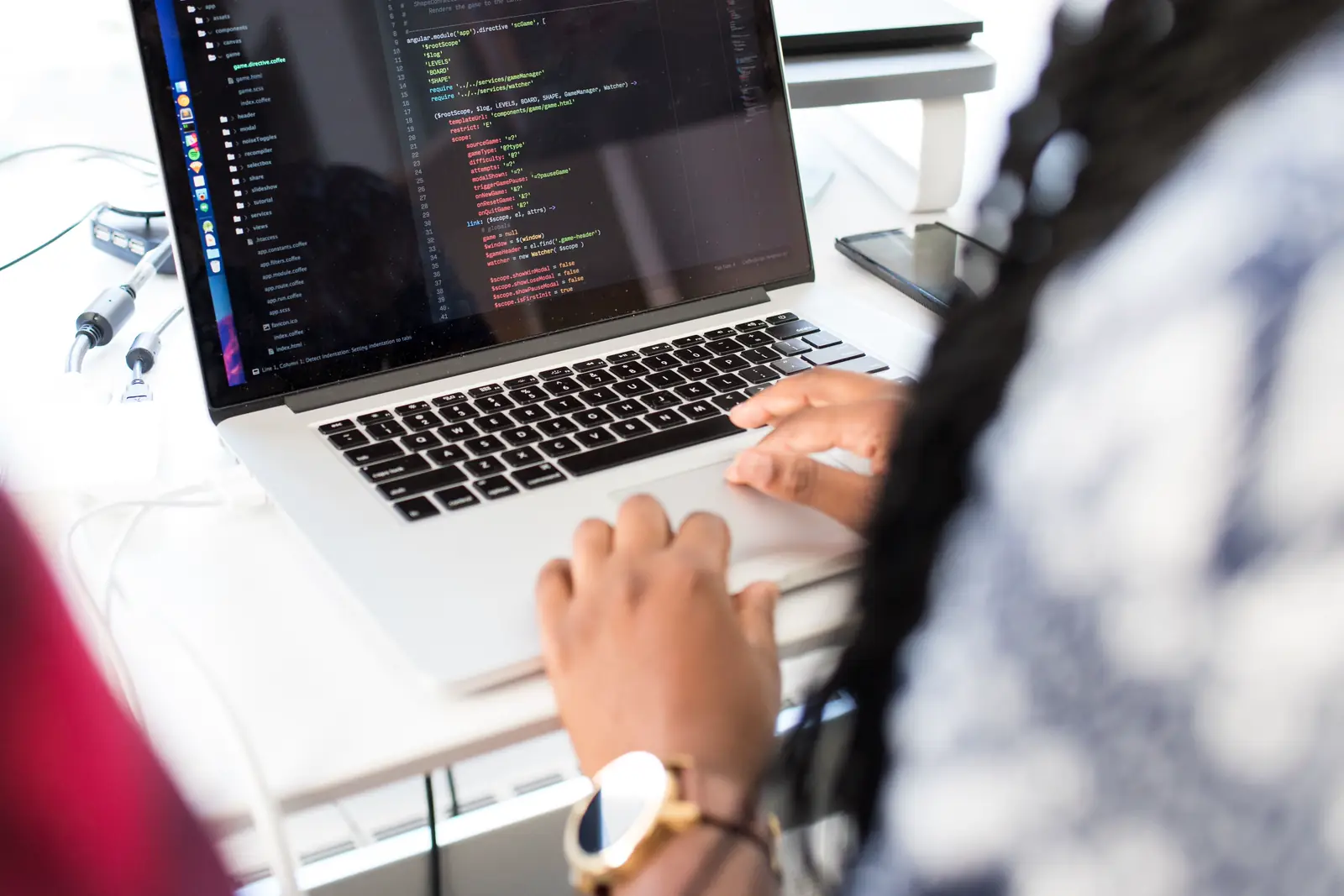 A woman at a desk writing code on a laptop, a website open on the screen.