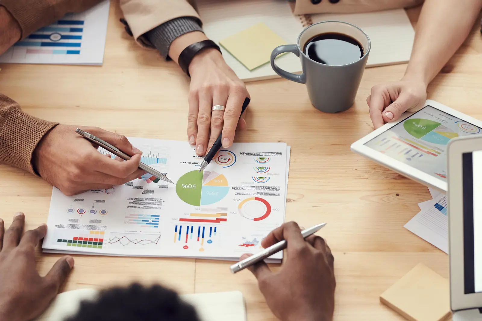 Colleagues around a table of printed charts, a coffee cup to one side.